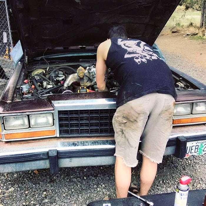 male working on car wearing tattoo style eagle and pinup tank top.