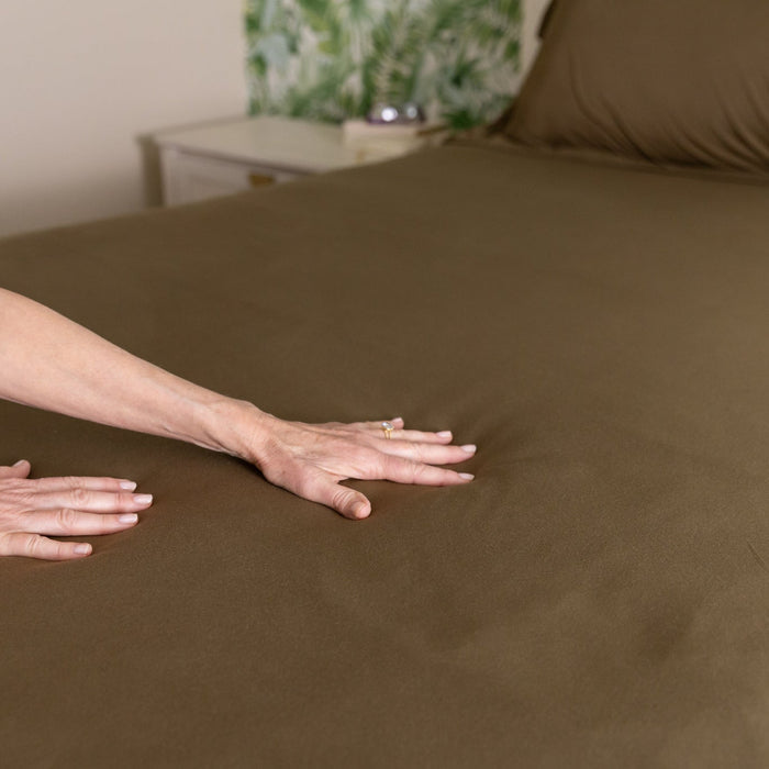 Person smoothing out a forest green duvet cover sheet on a bed