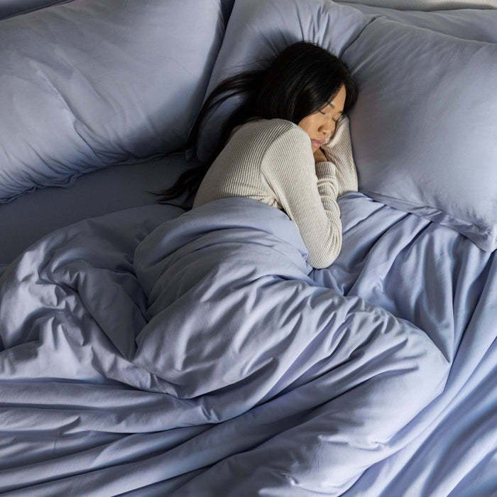 Person lying in bed under a light blue comforter