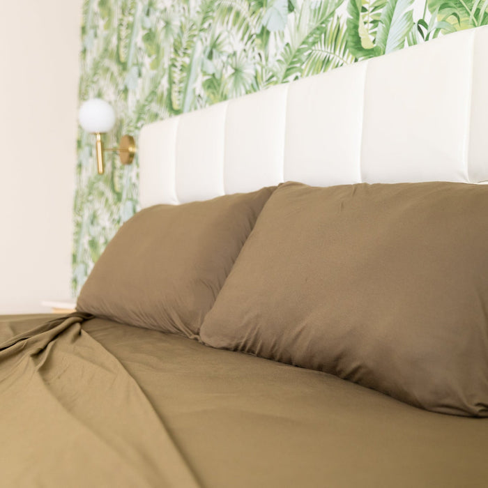Brown bed sheets on a bed with a white headboard and floral wallpaper.