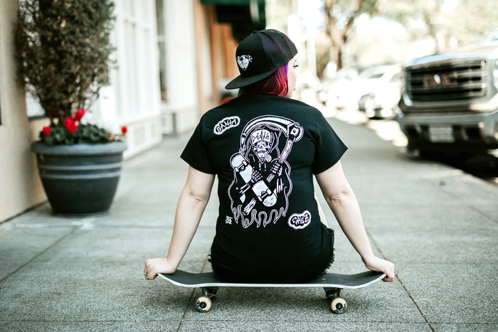 Female model sitting on skateboarding wearing tattoo style skateboard reaper t-shirt.
